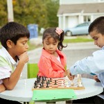 Young girl watches two young boys play chess
